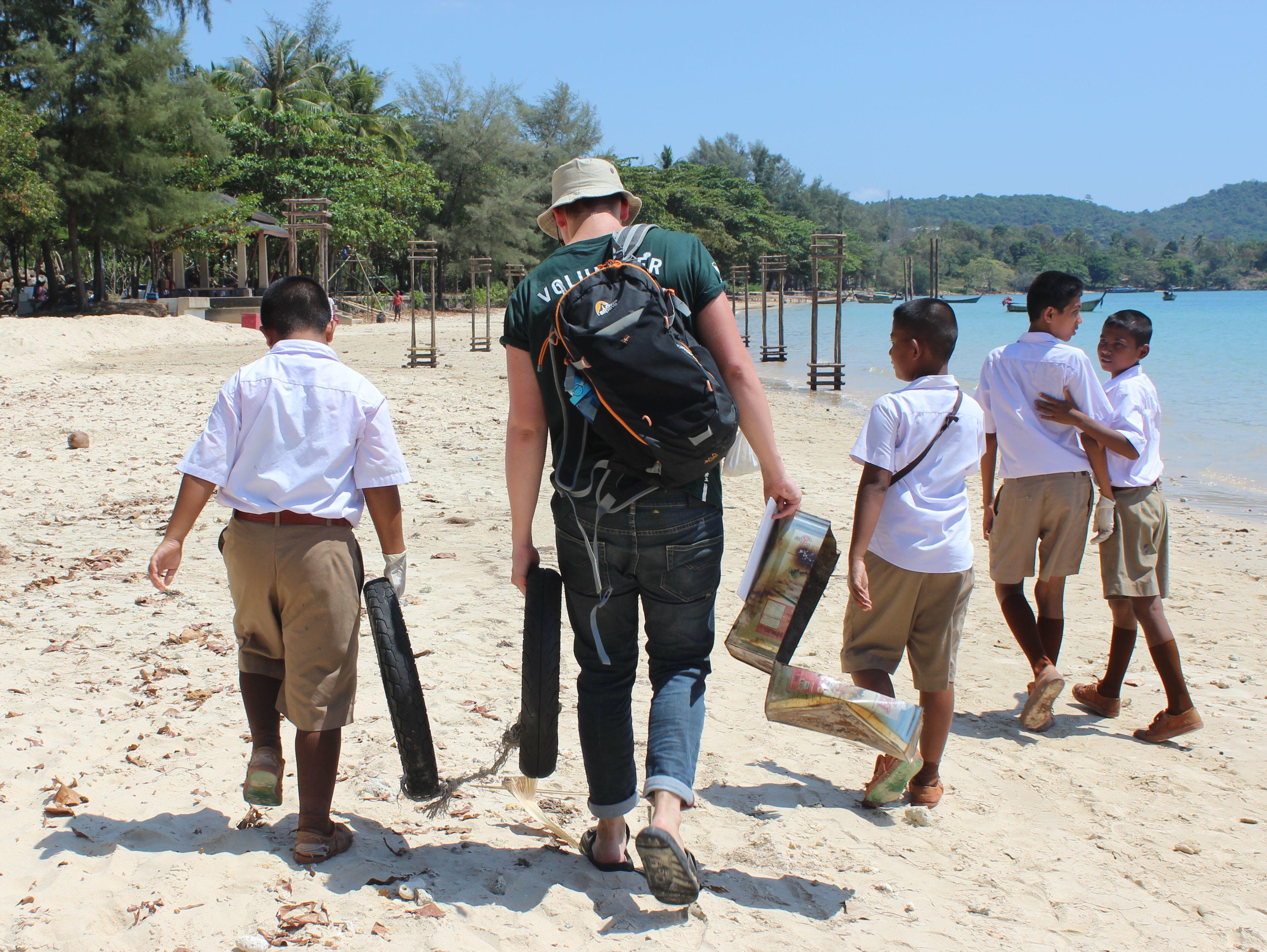 A Projects Abroad volunteer works with school children on a beach clean-up during his conservation volunteering in Thailand for high school students A high school student volunteer picks up litter on the beach to promote marine conservation in Thailand
